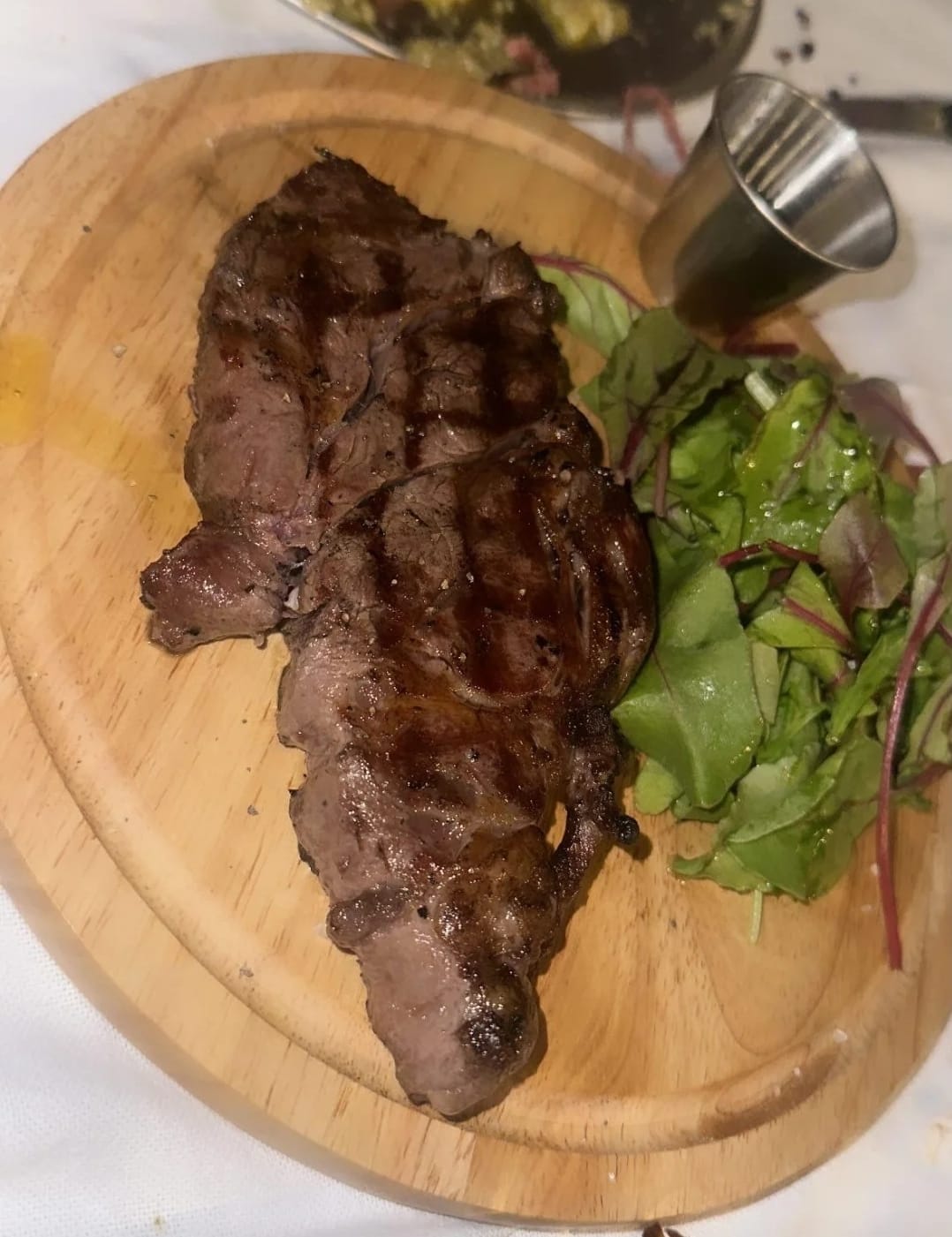 Grilled steak served on a wooden board with green salad at Rancho Asado