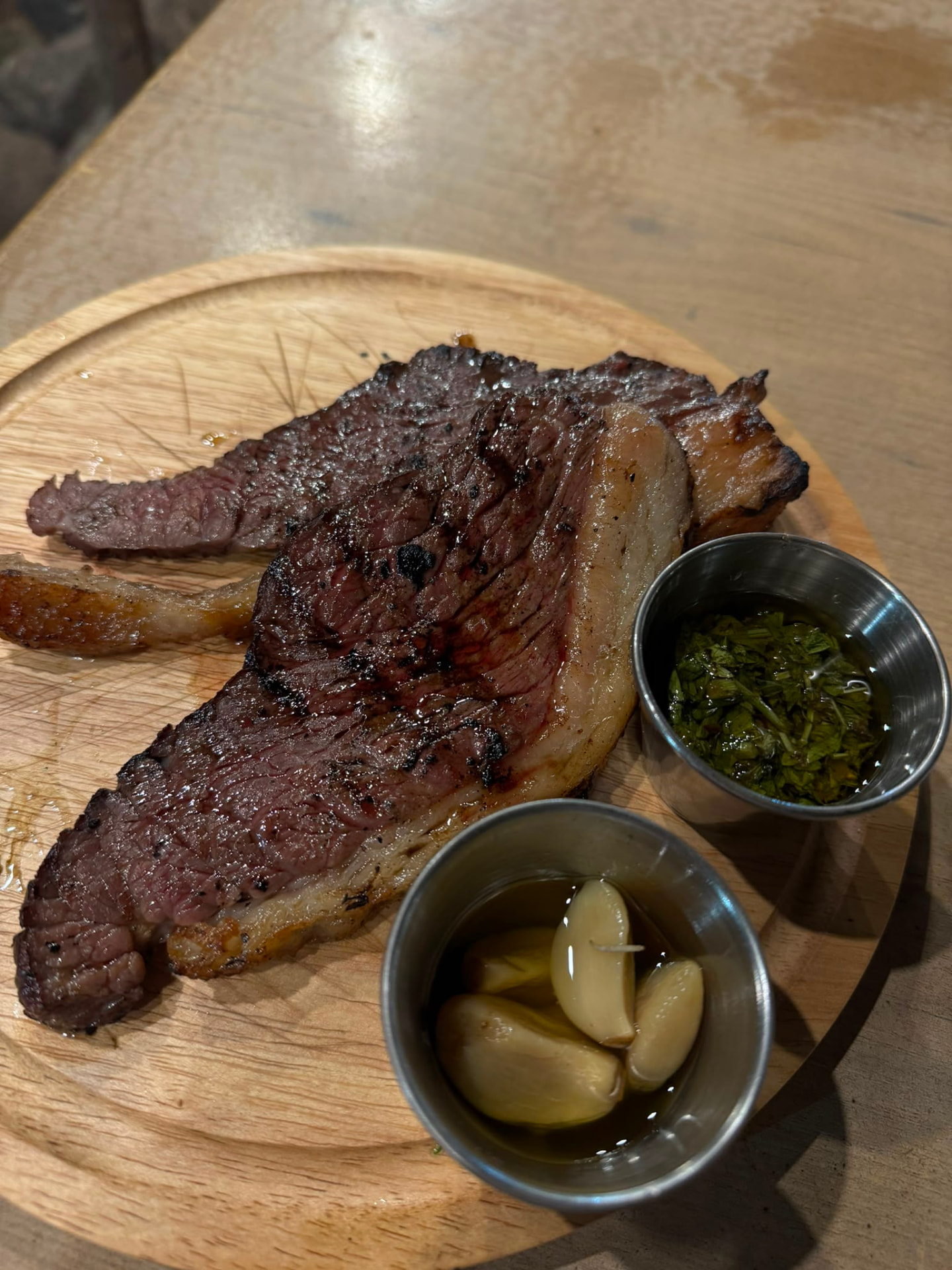 Grilled entrecote on a wooden board with chimichurri and confit garlic